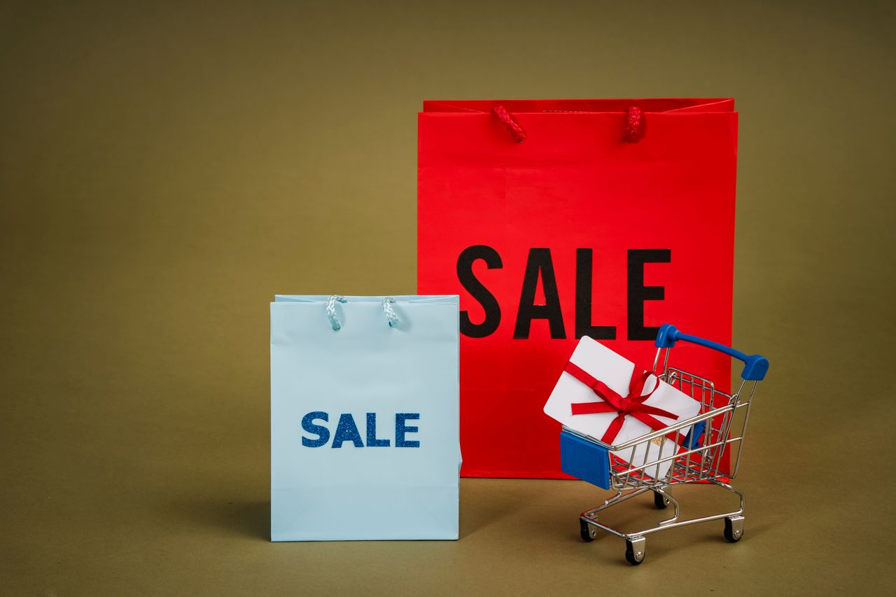 Home Bright sale bags with a gift in a shopping cart against a neutral background.